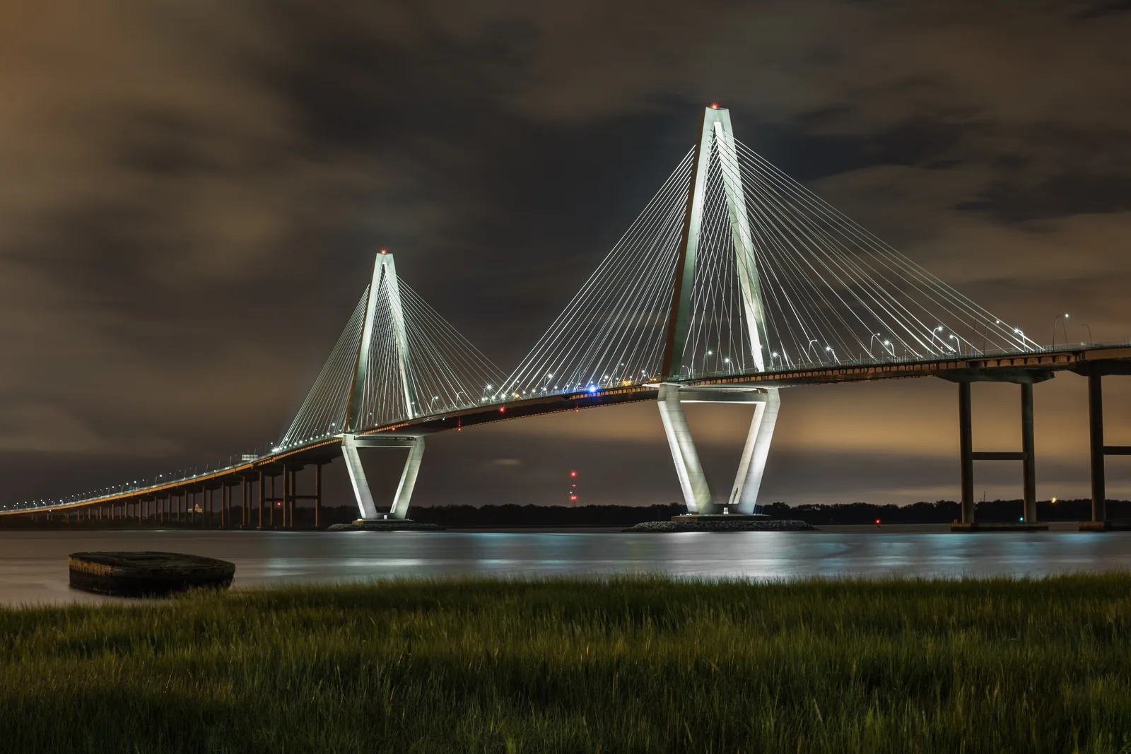 The Arthur Ravenel Jr. Bridge lit up over the Cooper River at night, seen from Mount Pleasant.