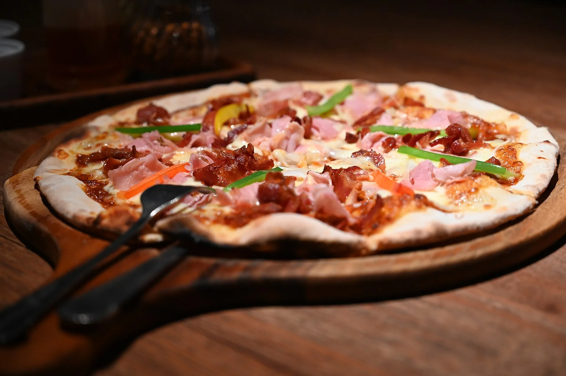 A wood-fired pizza with ham, herbs and melted cheese on a wooden board, a stock photograph not taken at a Charleston restaurant.